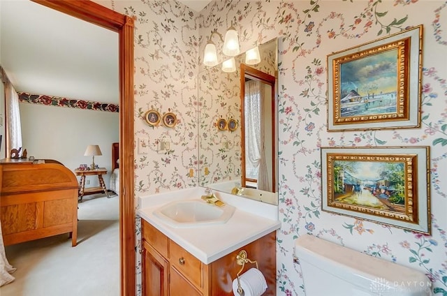 bathroom with toilet, vanity, and wallpapered walls