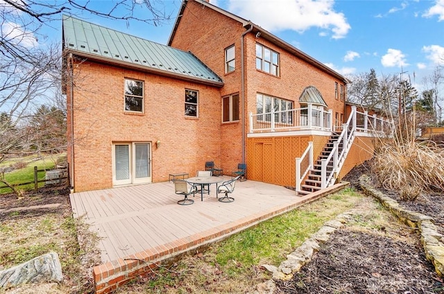 back of house featuring a standing seam roof, a wooden deck, metal roof, and brick siding