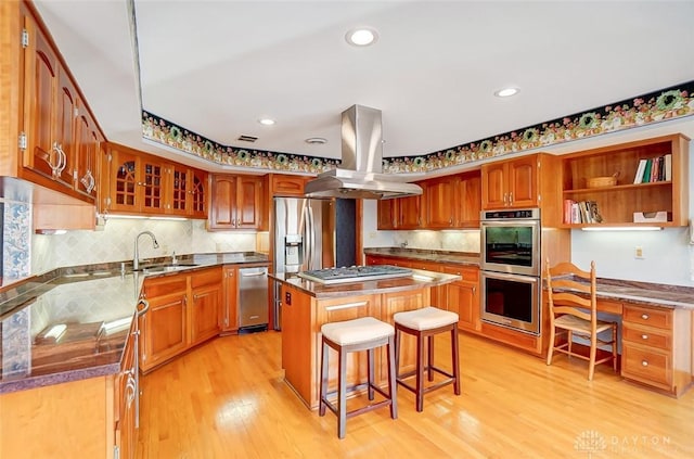 kitchen featuring stainless steel appliances, a sink, a kitchen island, light wood-style floors, and island exhaust hood