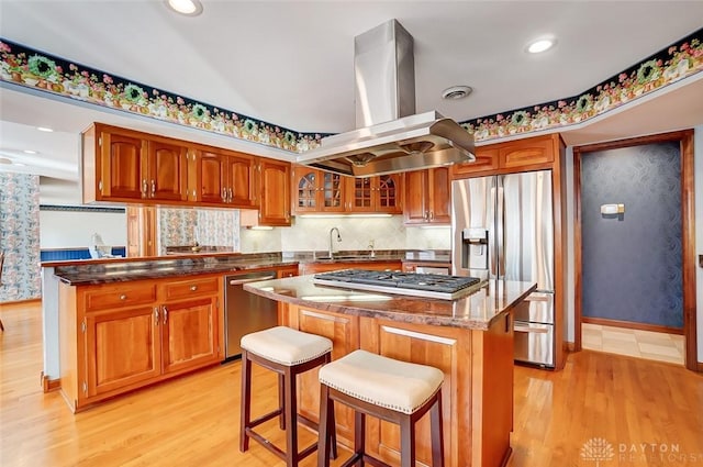 kitchen with appliances with stainless steel finishes, a center island, light wood-style floors, and island range hood