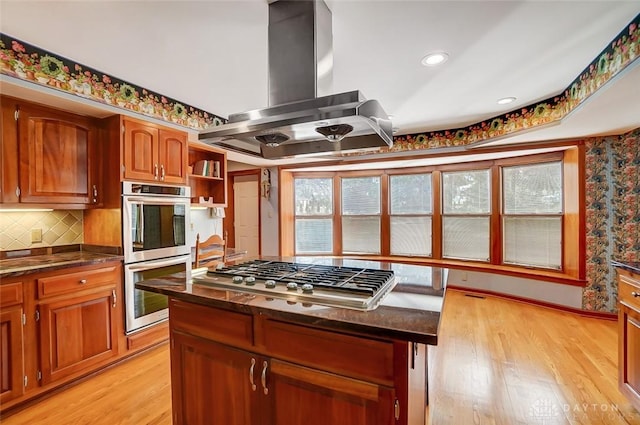 kitchen with stainless steel appliances, backsplash, light wood-type flooring, and island exhaust hood