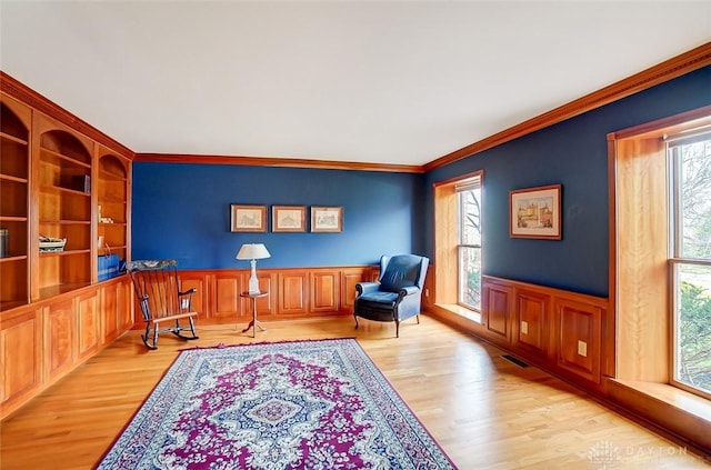 living area with ornamental molding, a wealth of natural light, a wainscoted wall, and light wood finished floors