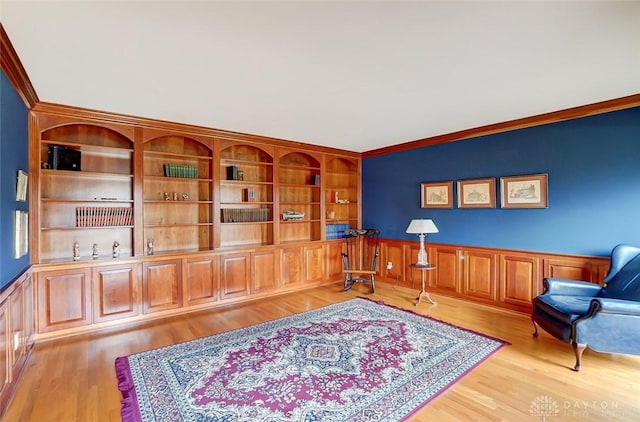 living area with a wainscoted wall, light wood-style flooring, and crown molding