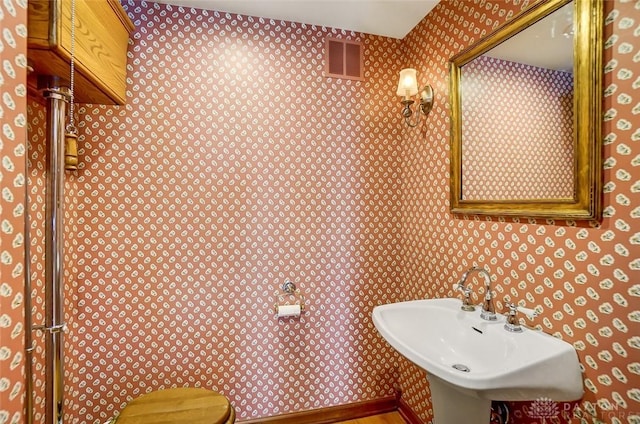 bathroom with baseboards, a sink, visible vents, and wallpapered walls