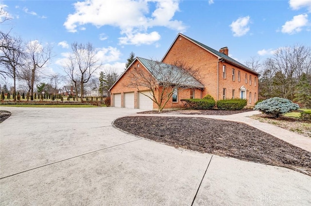 view of property exterior featuring a garage, concrete driveway, brick siding, and a chimney