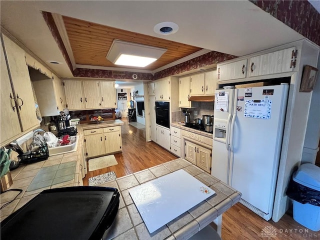 kitchen with black appliances, light wood-style flooring, tile counters, and tasteful backsplash