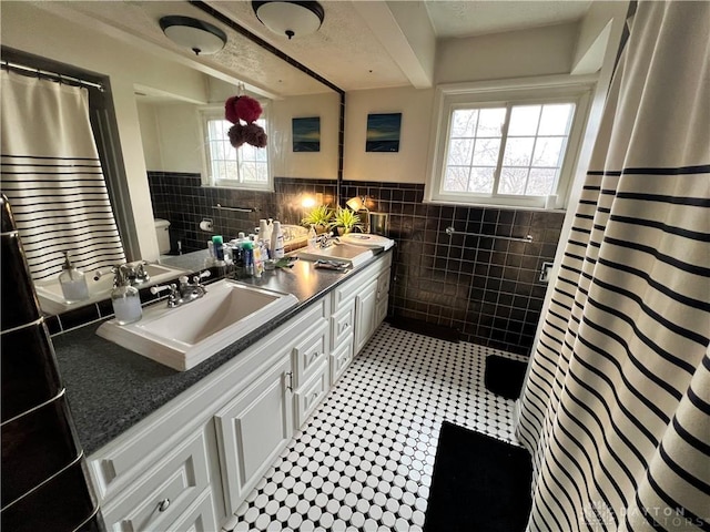 bathroom featuring double vanity, toilet, a wainscoted wall, a sink, and tile walls