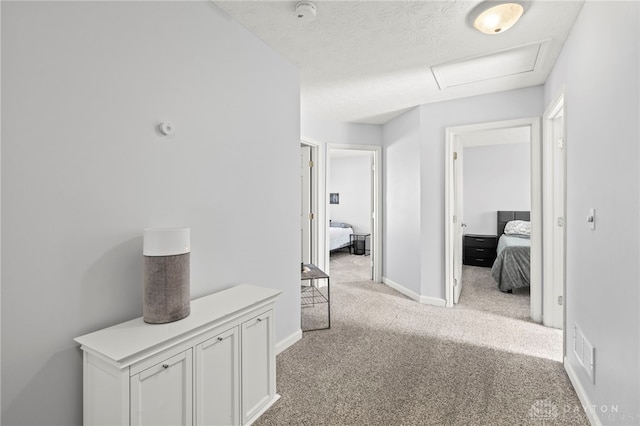 corridor with light carpet, attic access, visible vents, baseboards, and a textured ceiling