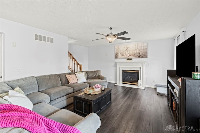 living room with dark wood-style flooring, visible vents, a glass covered fireplace, a textured ceiling, and stairs