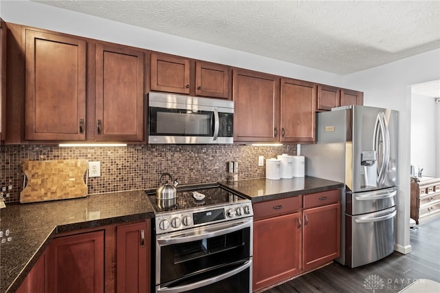 kitchen featuring appliances with stainless steel finishes, dark stone countertops, dark wood-style flooring, a textured ceiling, and backsplash