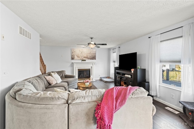 living room with ceiling fan, a glass covered fireplace, wood finished floors, and visible vents