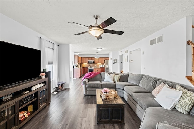 living room featuring dark wood-style floors, ceiling fan, visible vents, and a textured ceiling