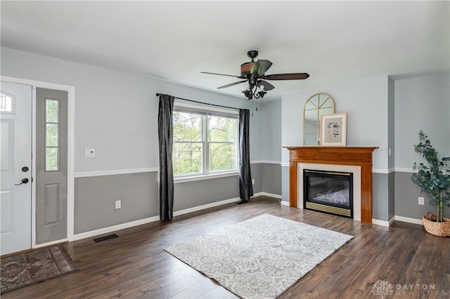 living area featuring wood finished floors, a ceiling fan, visible vents, baseboards, and a glass covered fireplace