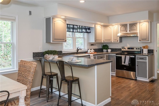 kitchen featuring under cabinet range hood, a peninsula, a breakfast bar, electric stove, and dark countertops