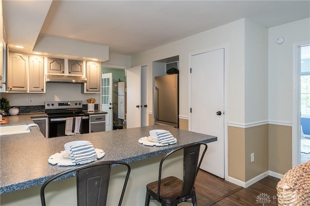 kitchen with a breakfast bar, appliances with stainless steel finishes, dark wood-type flooring, a peninsula, and under cabinet range hood