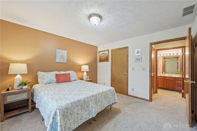 bedroom featuring visible vents, ensuite bathroom, light carpet, a textured ceiling, and baseboards