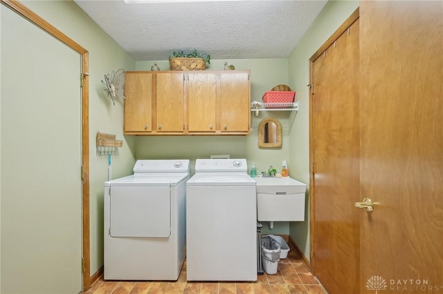 laundry area featuring a textured ceiling, washing machine and clothes dryer, cabinet space, and baseboards