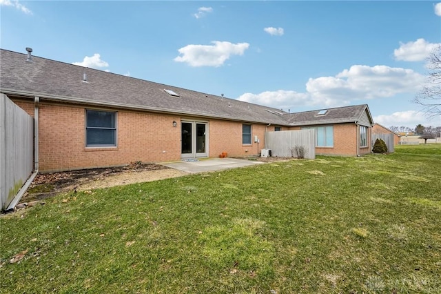 rear view of property featuring a patio, brick siding, fence, a yard, and roof with shingles