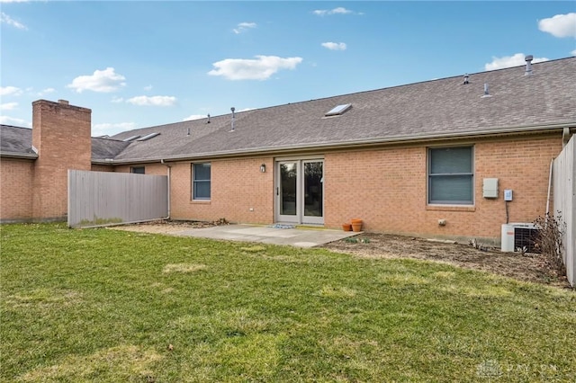 rear view of property featuring central AC unit, a lawn, a shingled roof, and fence