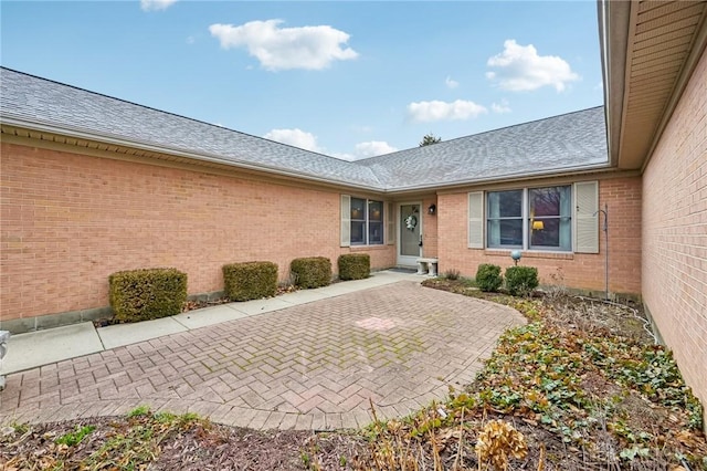 view of exterior entry featuring a shingled roof and brick siding