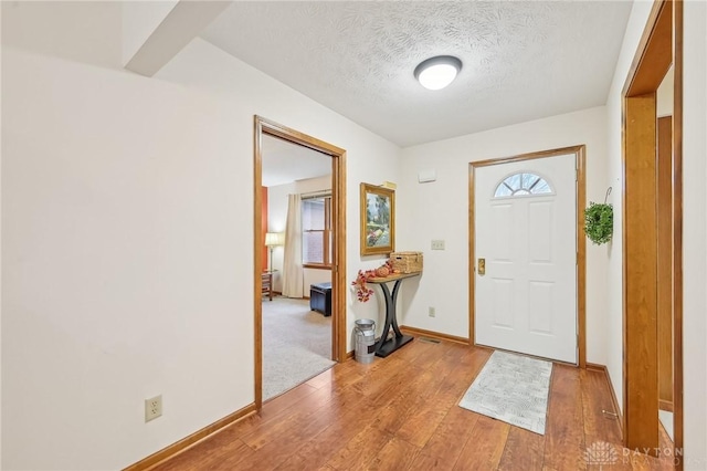 foyer entrance with a textured ceiling, baseboards, and light wood-style floors