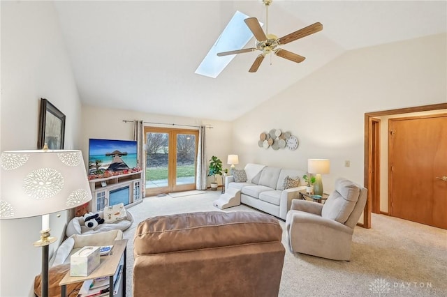 carpeted living room with a ceiling fan, vaulted ceiling with skylight, and french doors