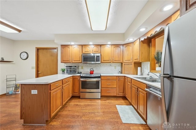 kitchen with backsplash, appliances with stainless steel finishes, a sink, light wood-type flooring, and a peninsula