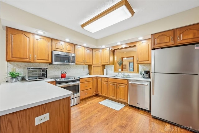 kitchen featuring light wood finished floors, appliances with stainless steel finishes, light countertops, and a sink