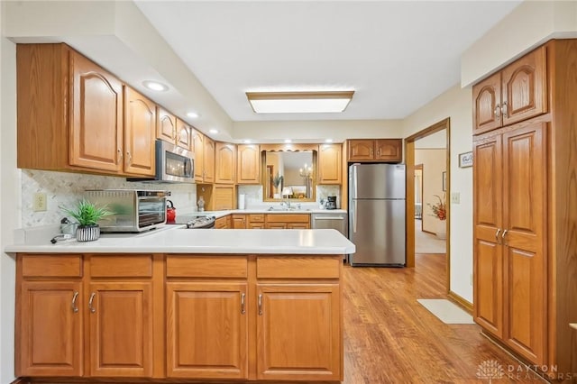 kitchen with a peninsula, light wood-style floors, appliances with stainless steel finishes, and light countertops