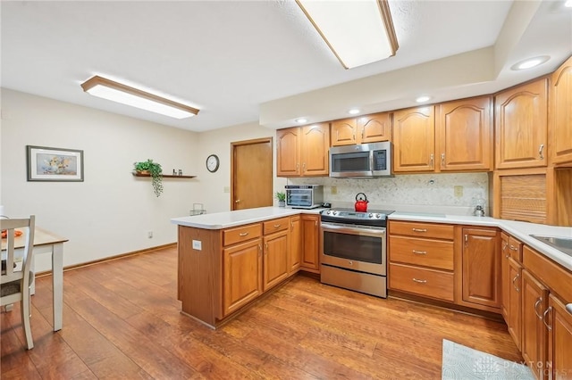 kitchen with light countertops, decorative backsplash, appliances with stainless steel finishes, light wood-type flooring, and a peninsula