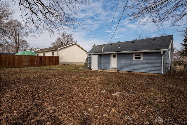 rear view of house featuring roof with shingles and fence