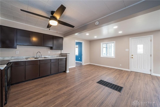 kitchen featuring dark brown cabinetry, baseboards, wood finished floors, light countertops, and a sink