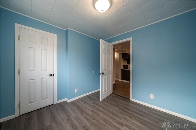 unfurnished bedroom featuring baseboards, wood finished floors, and ornamental molding