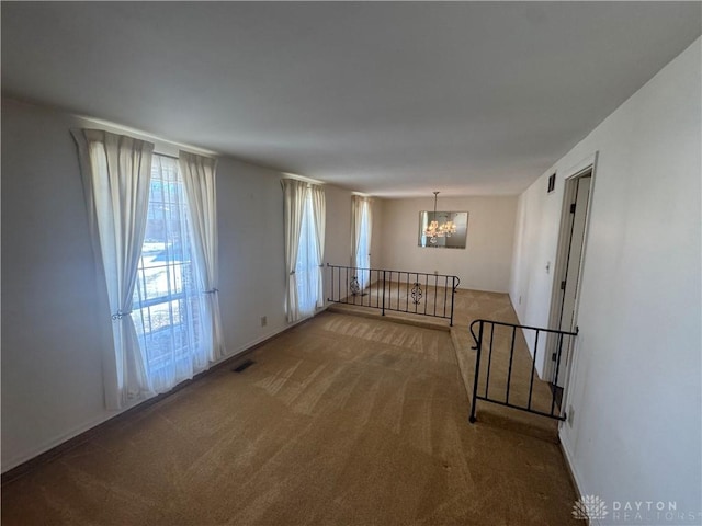 carpeted empty room with visible vents and a notable chandelier