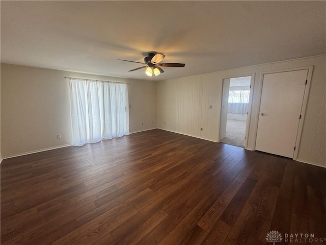 empty room featuring a ceiling fan, dark wood finished floors, and baseboards