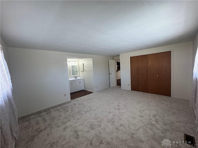 unfurnished bedroom featuring carpet floors, a closet, and ensuite bath