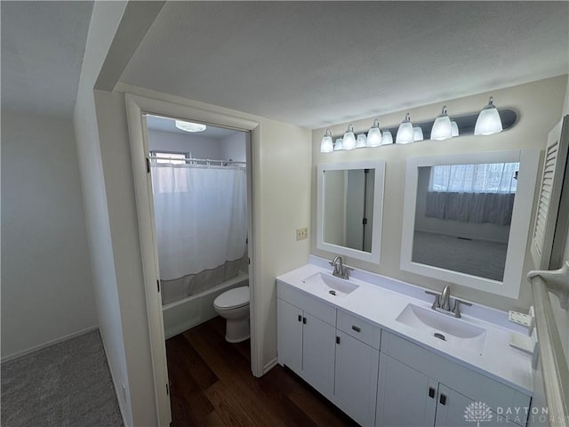 bathroom with wood finished floors, a sink, toilet, and double vanity