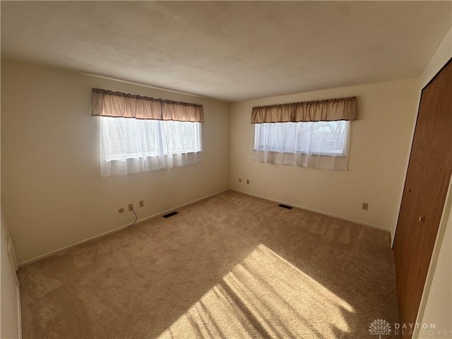 carpeted empty room featuring baseboards and visible vents