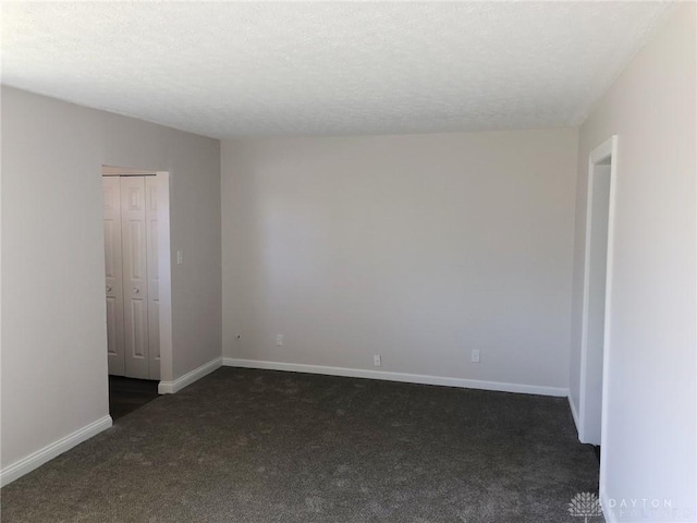 spare room featuring baseboards, dark colored carpet, and a textured ceiling