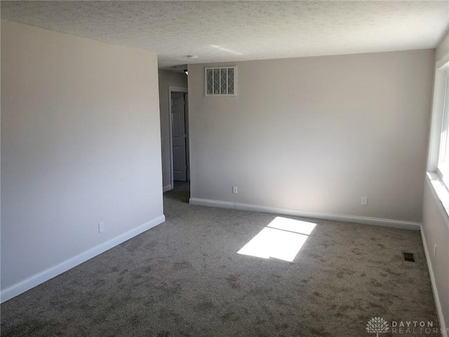 spare room featuring a textured ceiling, carpet flooring, visible vents, and baseboards