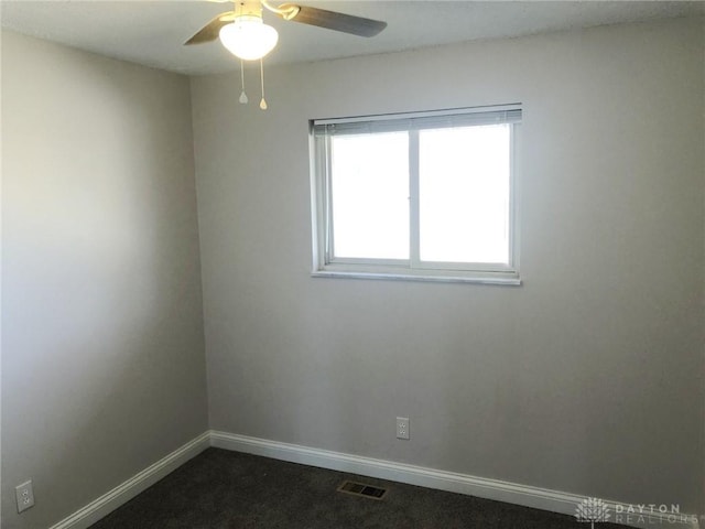 empty room with dark colored carpet, a ceiling fan, visible vents, and baseboards