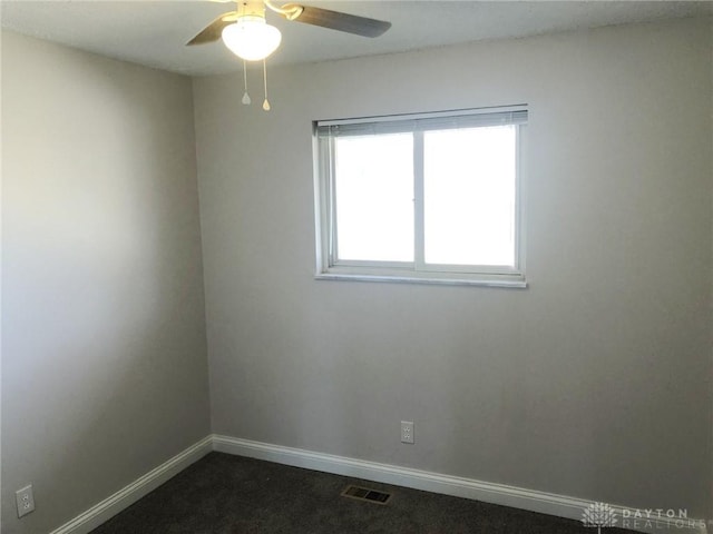 spare room with baseboards, ceiling fan, visible vents, and dark colored carpet