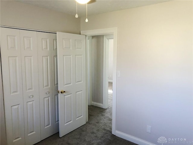 unfurnished bedroom with a closet, dark carpet, and baseboards