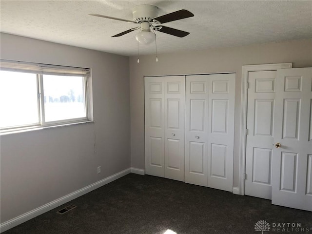 unfurnished bedroom featuring dark colored carpet, a closet, visible vents, a textured ceiling, and baseboards