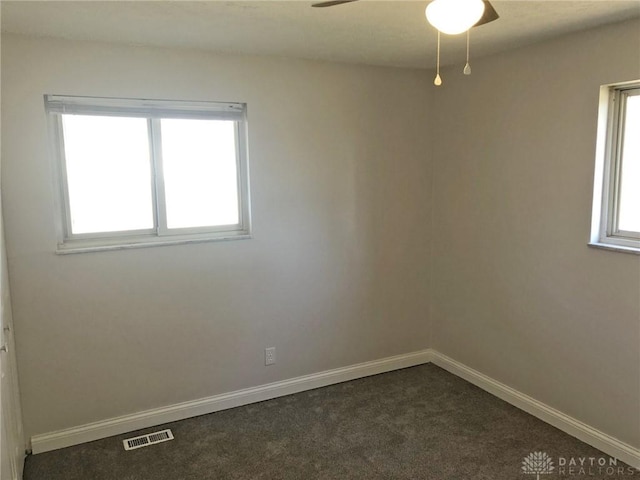 empty room featuring baseboards, visible vents, dark colored carpet, and a ceiling fan