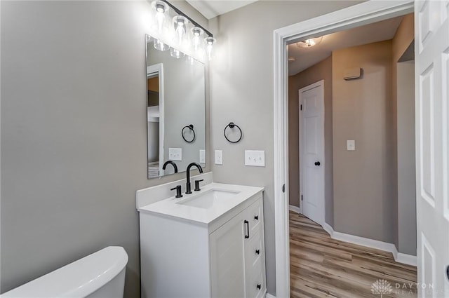 bathroom with toilet, wood finished floors, vanity, and baseboards