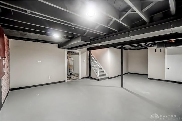 finished basement featuring brick wall, stairs, water heater, and baseboards