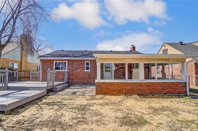 back of house featuring a sunroom, a chimney, fence, a deck, and brick siding