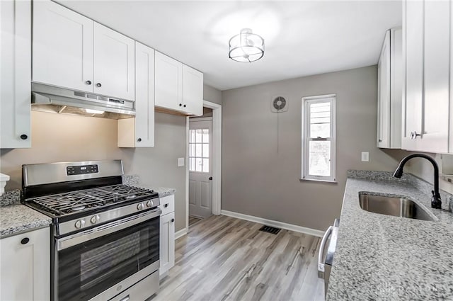 kitchen featuring stainless steel gas stove, plenty of natural light, a sink, and under cabinet range hood