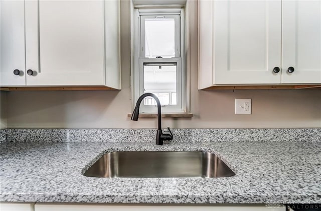 kitchen featuring a sink, light stone countertops, and white cabinets